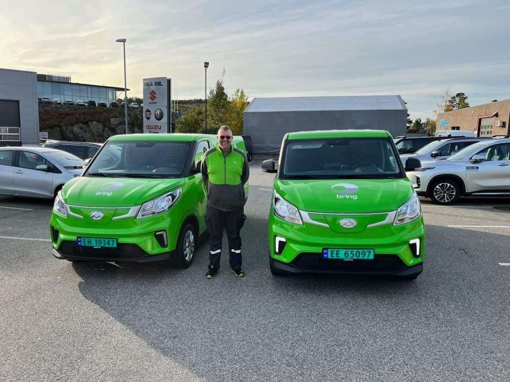 To grønne elektriske budbiler fra Bring parkert med sjåfør i uniform. Del av tredjepartslogistikk og samarbeid med Stortuen Transport i Agder.